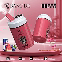 Two pink Bang De disposable vape devices with a monkey wearing a jeweled crown illustration, advertised for 60,000 puffs, featuring Blueberry Watermelon and Red Bull flavors, with icons for three flavors, dual coil, intelligent power indicator, and digital oil indicator on a pink gradient background.
