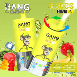 Deux dispositifs de vape jetables 3-en-1 à Bang Yellow avec une saveur de glace de banane, montrant un singe de dessin animé portant des lunettes de soleil et une casquette jaune, entourée de glaçons, des tranches de pastèque, des ours gommeux, une fraise et des bananes, contre un fond vert avec du texte mettant en évidence 8500 bouffées et le flux d'air triple.