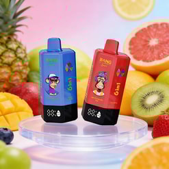 Two boxy vape devices, blue and red, with cartoon monkey faces, standing on a clear pedestal amid a fruit-filled background.