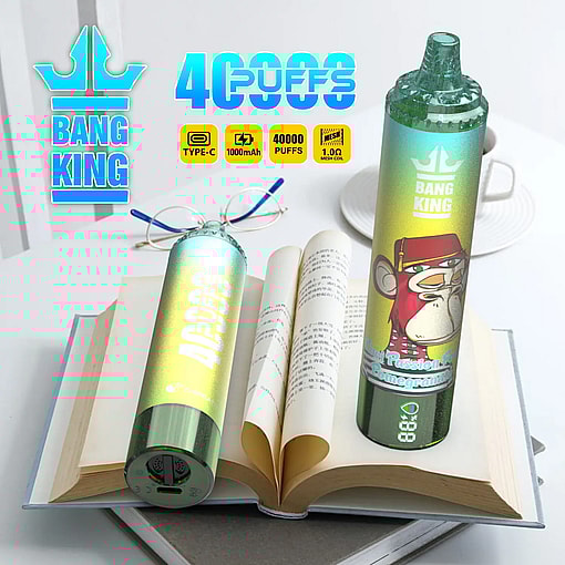 Two colorful Bang King disposable vape devices with a monkey illustration, placed on top of an open book with text in an Asian language, next to a pair of glasses and a white cup on a saucer.
